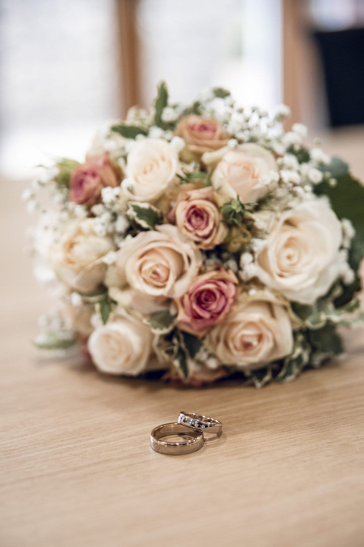 Eine Nahaufnahme vom hellen Brautstrauß und Ringe auf einem Holztisch.