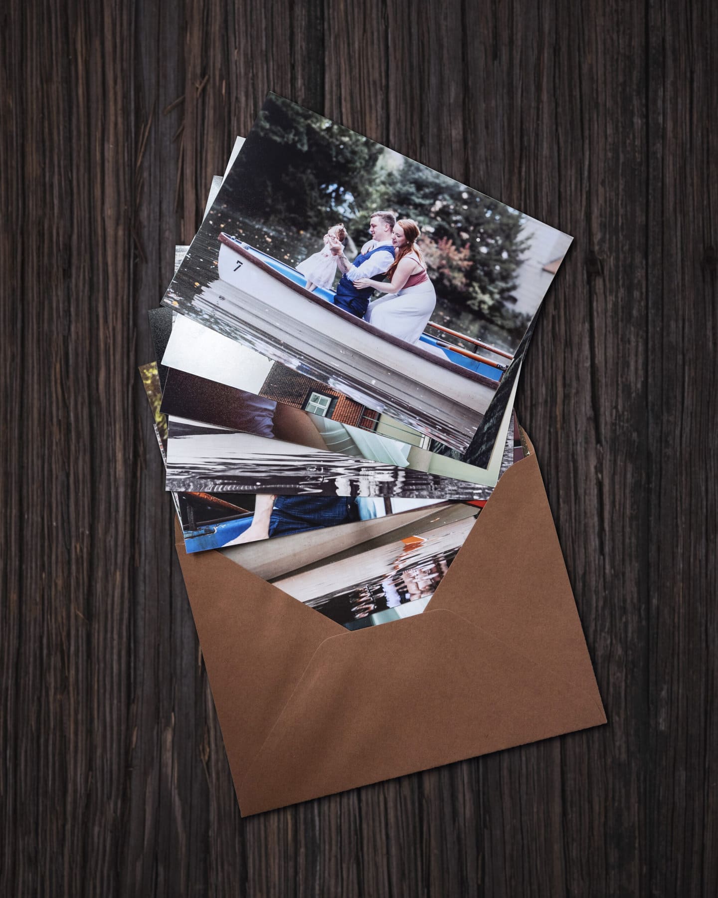 Die Hochzeitsfotos als Abzüge in einem Kuvert auf einem Holztisch.