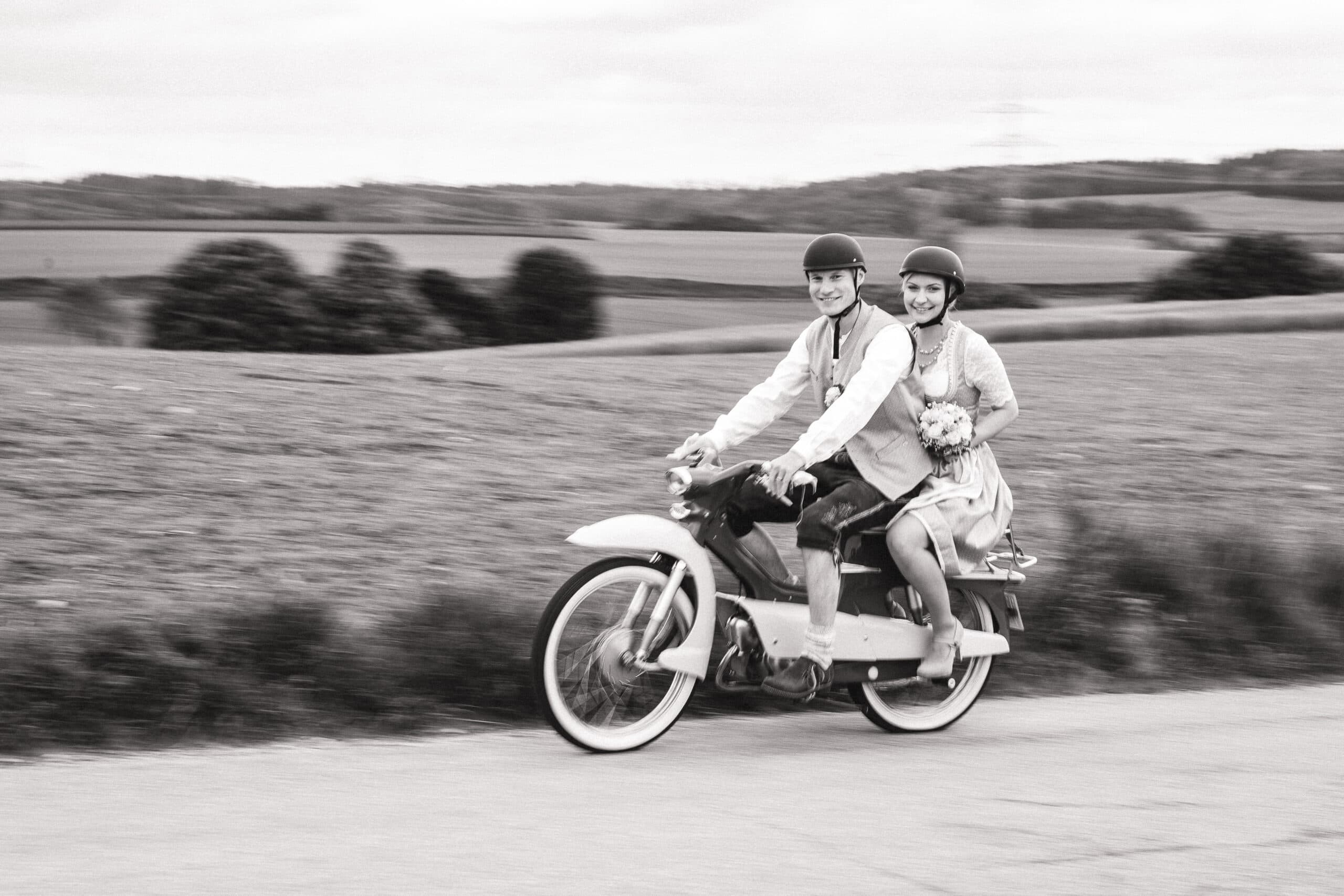Eine Aufnahme in schwarz-weiß. Das Brautpaar fährt mit dem Moped zum Standesamt in Aindling.