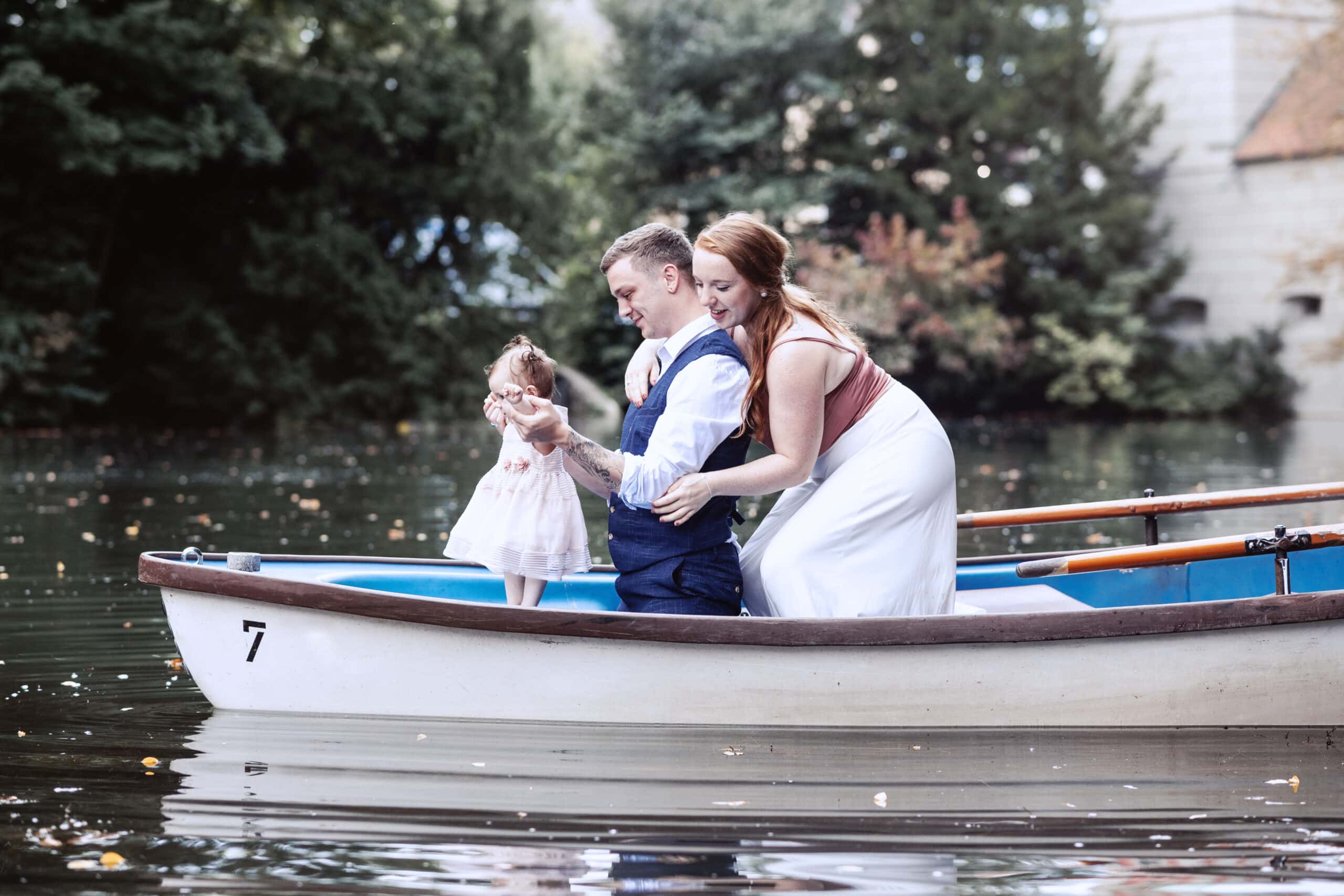 Das After Wedding Shooting in Augsburg. Das Brautpaar sitzt und spielt mit ihrem Kind in einem Ruderboot.