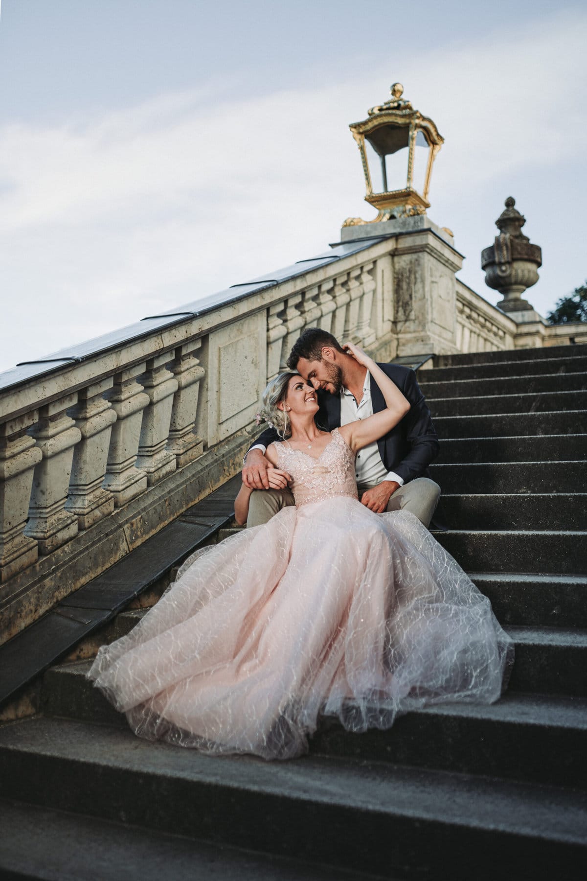 Ein Hochzeitsfoto vom Brautpaar auf den Stufen von Schloss Nymphenburg in München.