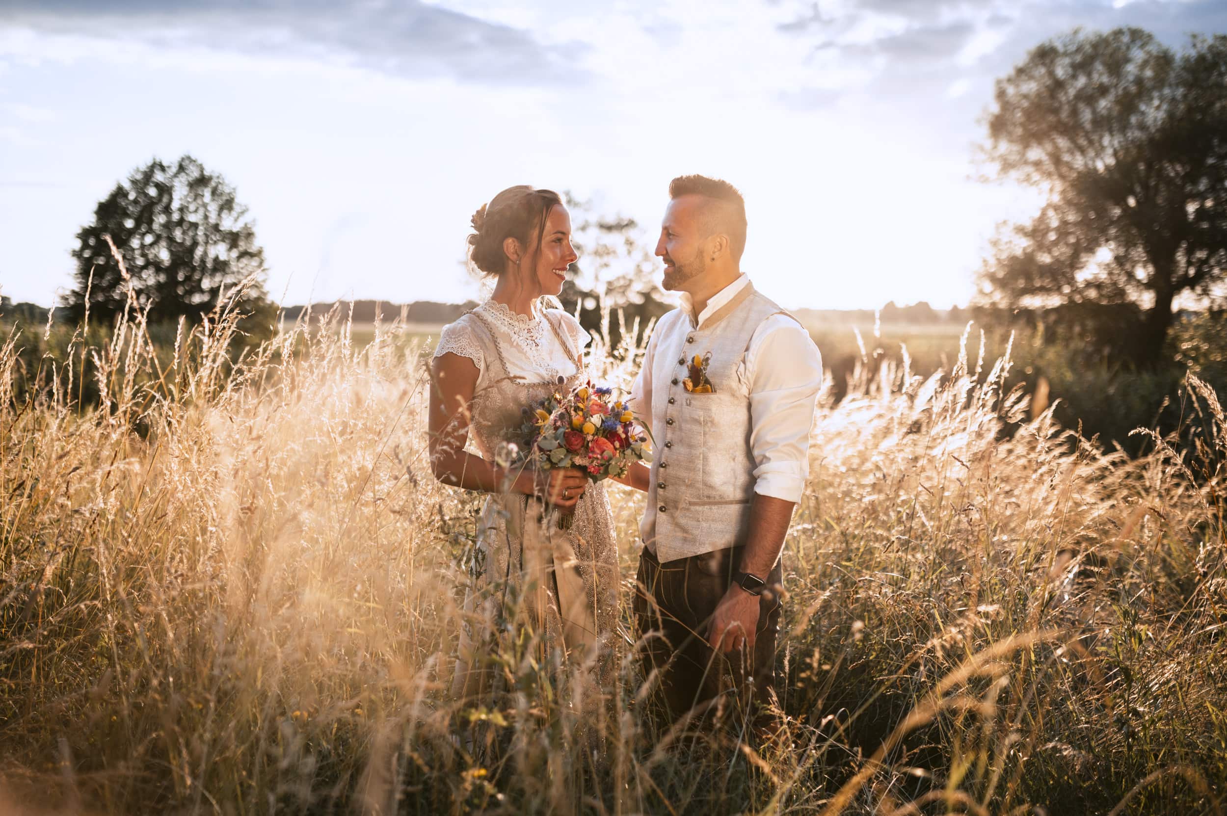 Das Brautpaar bei einem Hochzeitshooting in einem Feld mit hohem Gras in Thierhaupten beim Sonnenuntergang.