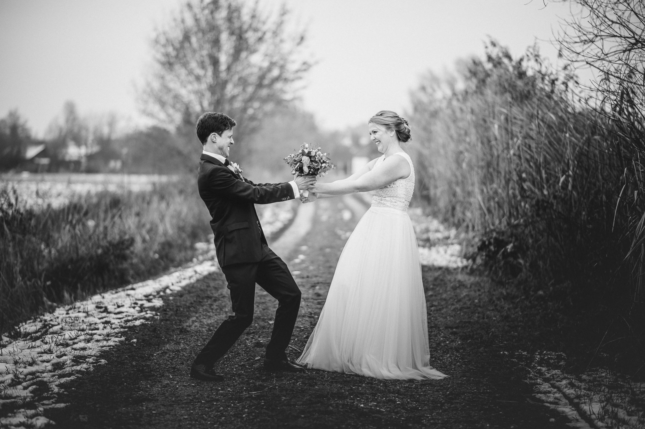 Eine Aufnahme in schwarz-weiß. Das Brautpaar kämpft beim Spaß-Foto um den Brautstrauß in Thierhaupten.