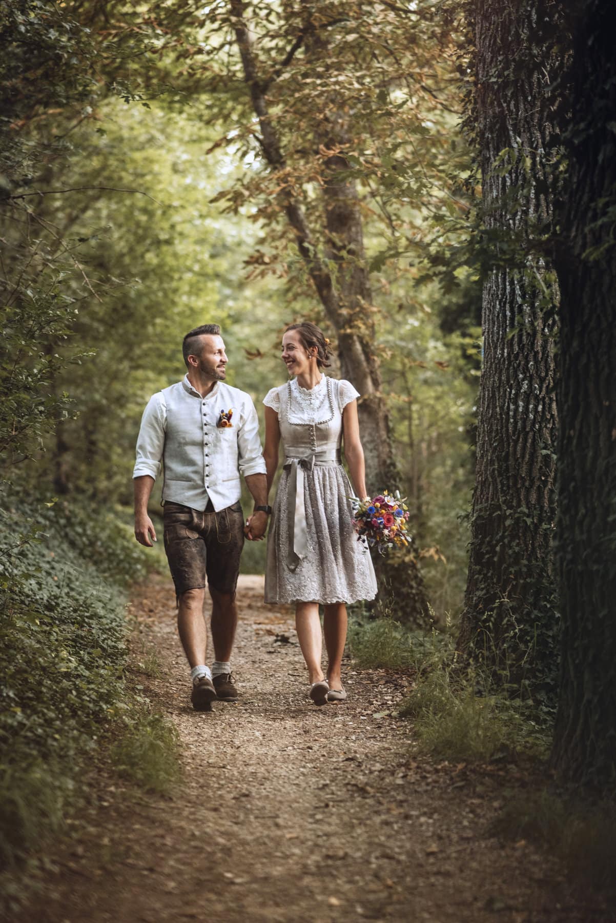 Das Hochzeitspaar beim Hochzeitshooting ist auf einem Weg im Wald spazieren in Thierhaupten.