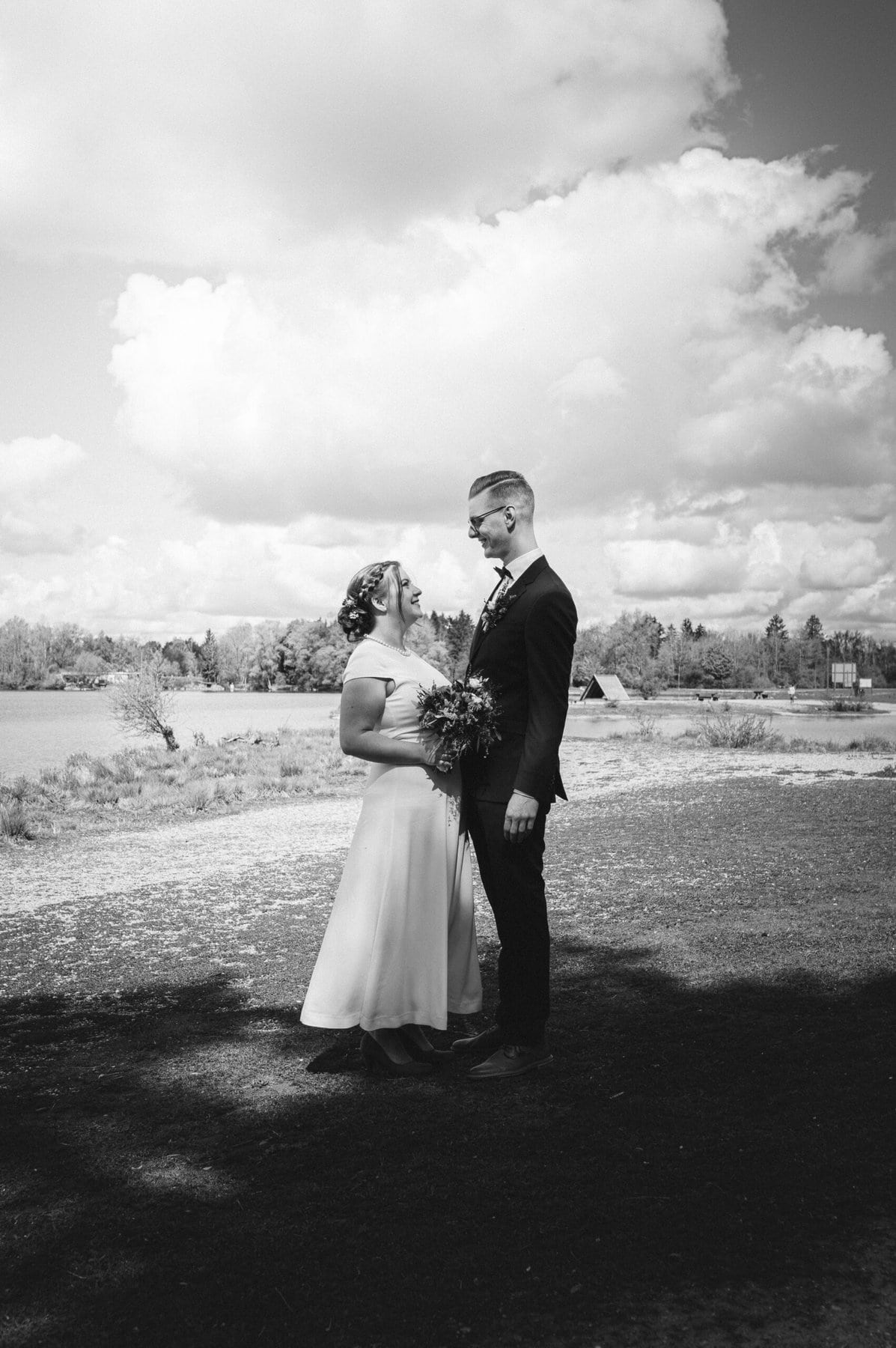 Ein Bild in schwarz-weiß. Das Brautpaar sieht sich an am Weitmannsee bei Kissing.