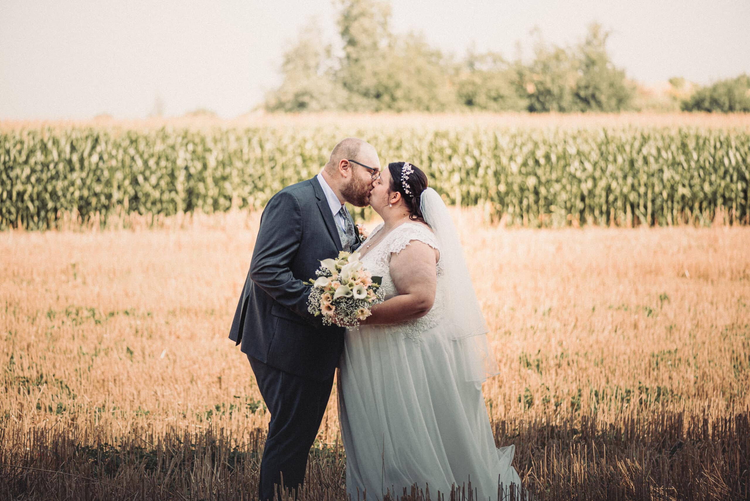 Das Brautpaar küsst sich beim Hochzeitsshooting in einem Feld in Gablingen.