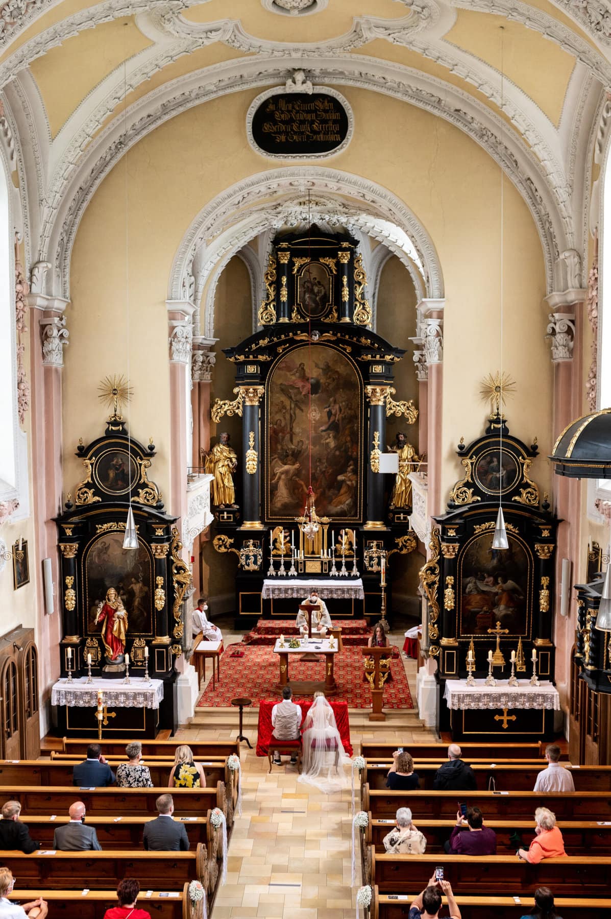 Eine Aufnahme von oben bei der Hochzeit in Affing. Das Brautpaar sitzt am Altar in der Kirche St. Peter und Paul in Affing.