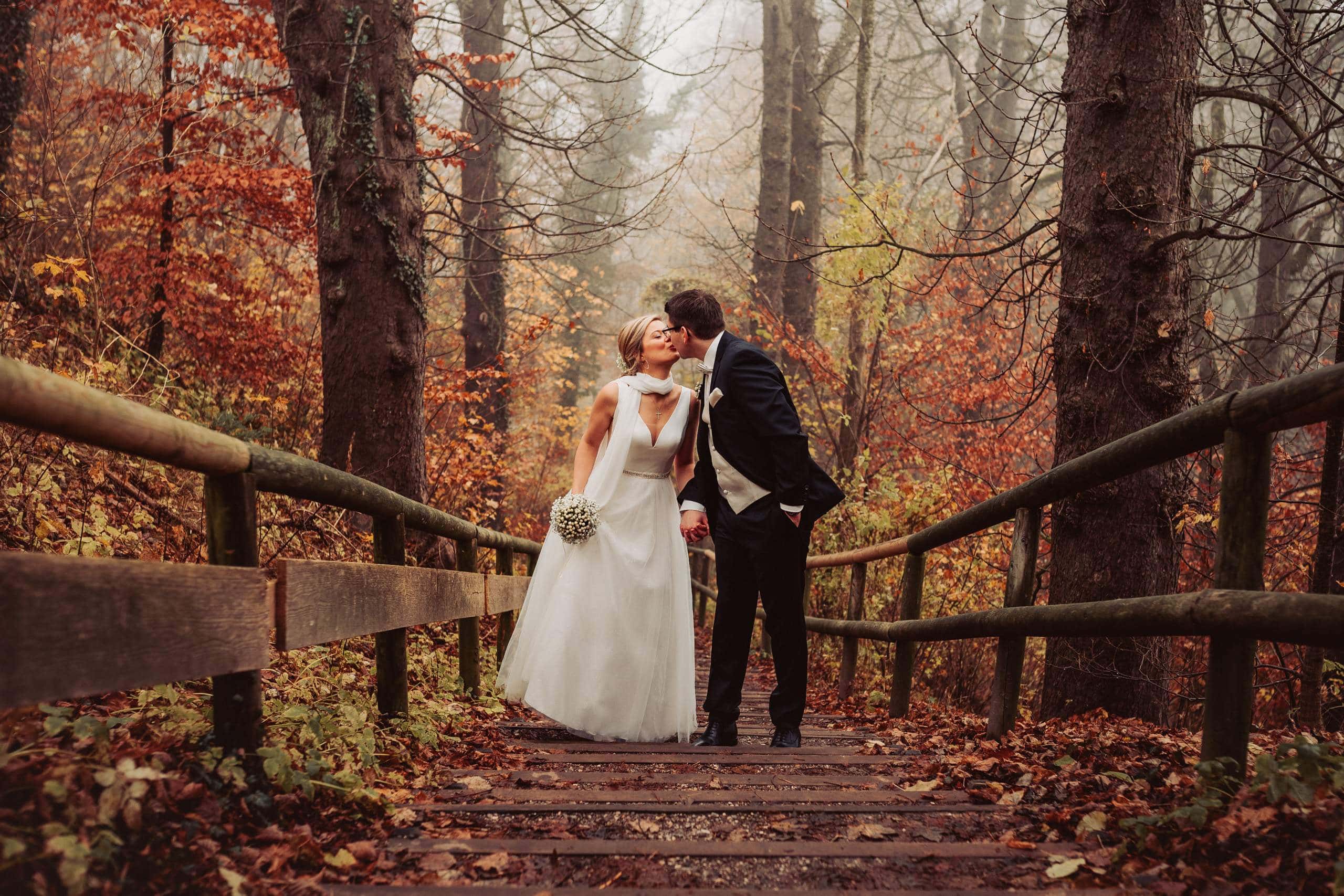 Im Brautpaarshooting küsst sich das Brautpaar im bunten Herbstwald.