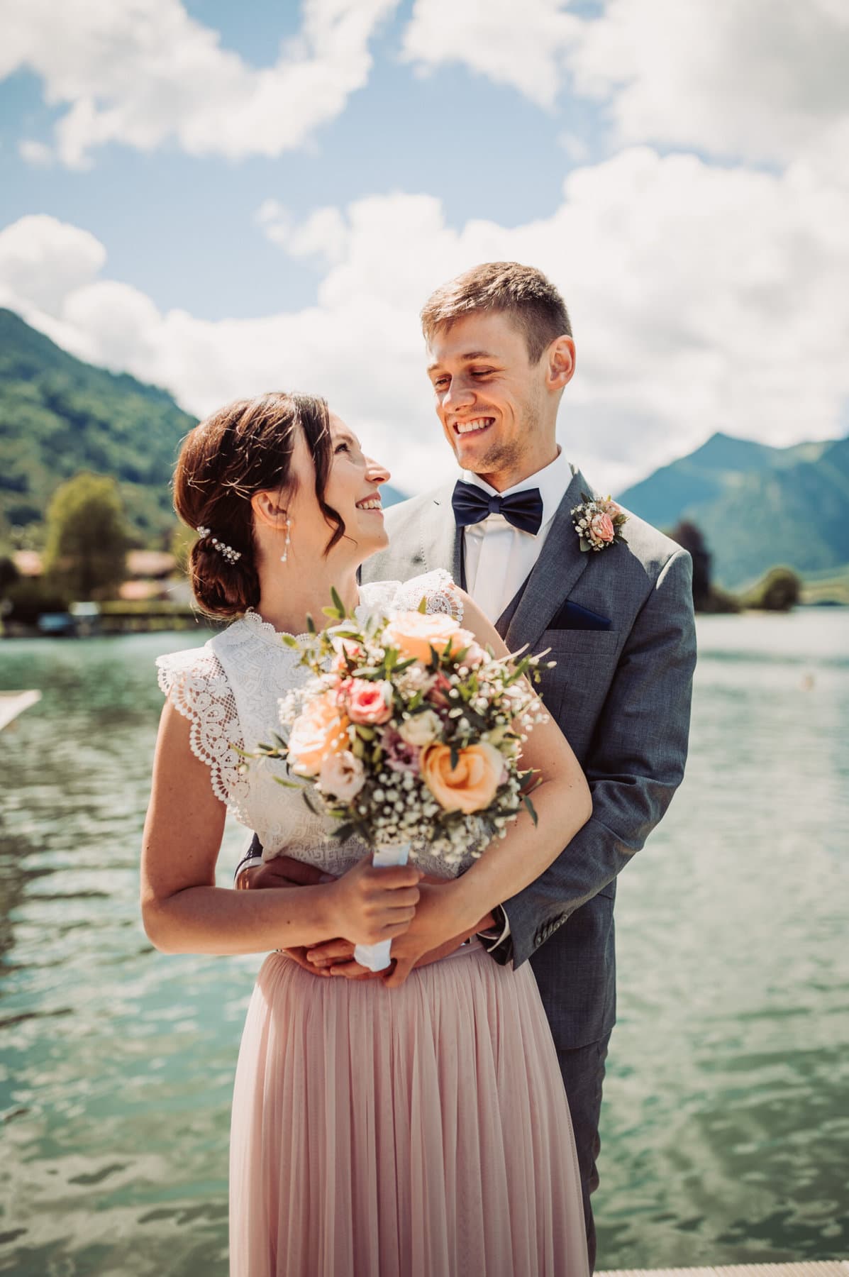 Das Hochzeitsshooting in Oberbayern am Schliersee. Das Brautpaar steht auf einem Steg und sehen sich in die Augen.