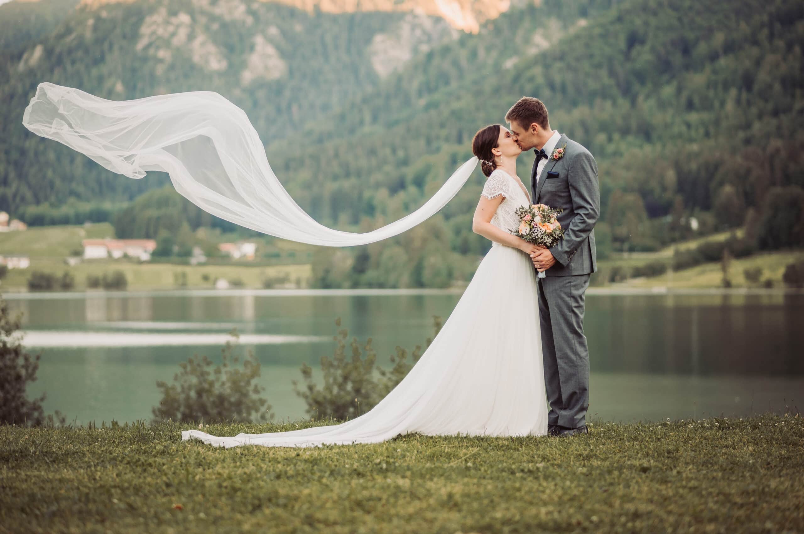Das Hochzeitsshooting in Oberbayern am Schliersee. Das Brautpaar steht auf der Insel und küsst sich mit fliegendem Schleier.