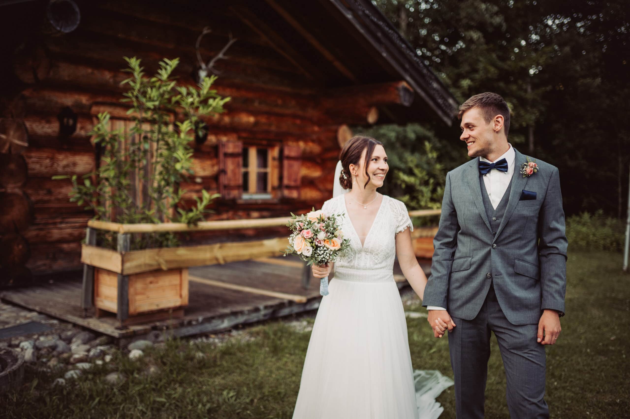 Das Hochzeitsshooting in Oberbayern am Schliersee. Das Brautpaar läuft vor einem Haus aus Holz.