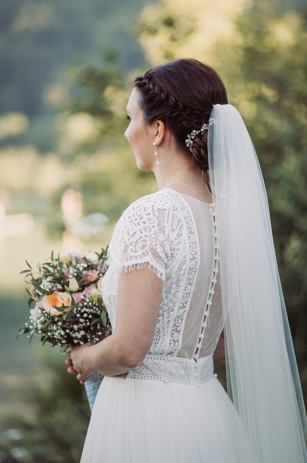 Das Hochzeitsshooting in Oberbayern am Schliersee. Die Braut steht von hinten, sodass man ihre Frisur und Schleier gut erkenne kann.