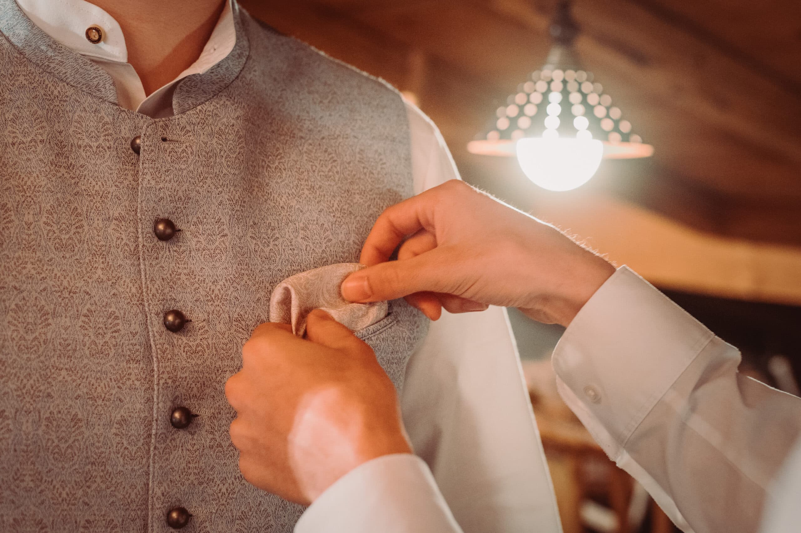 Das Getting Ready vom Bräutigam auf der Meckatzer Sportalp. Eine Nahaufnahme wie dem Bräutigam in die Tasche der Weste ein Tuch eingesteckt wird.