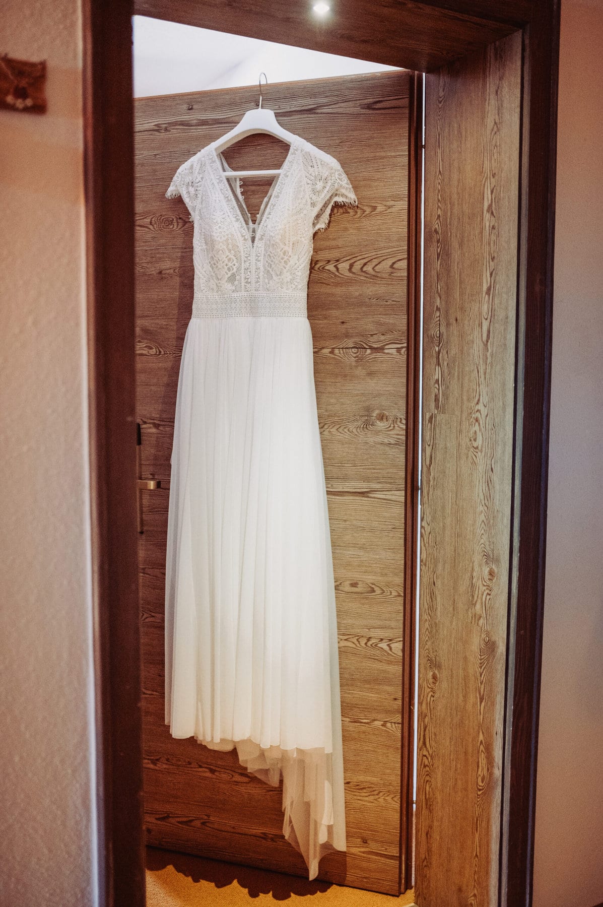 Das Getting Ready der Braut in Oberbayern am Schliersee. Das Hochzeitskleid hängt an einer offenen Tür.