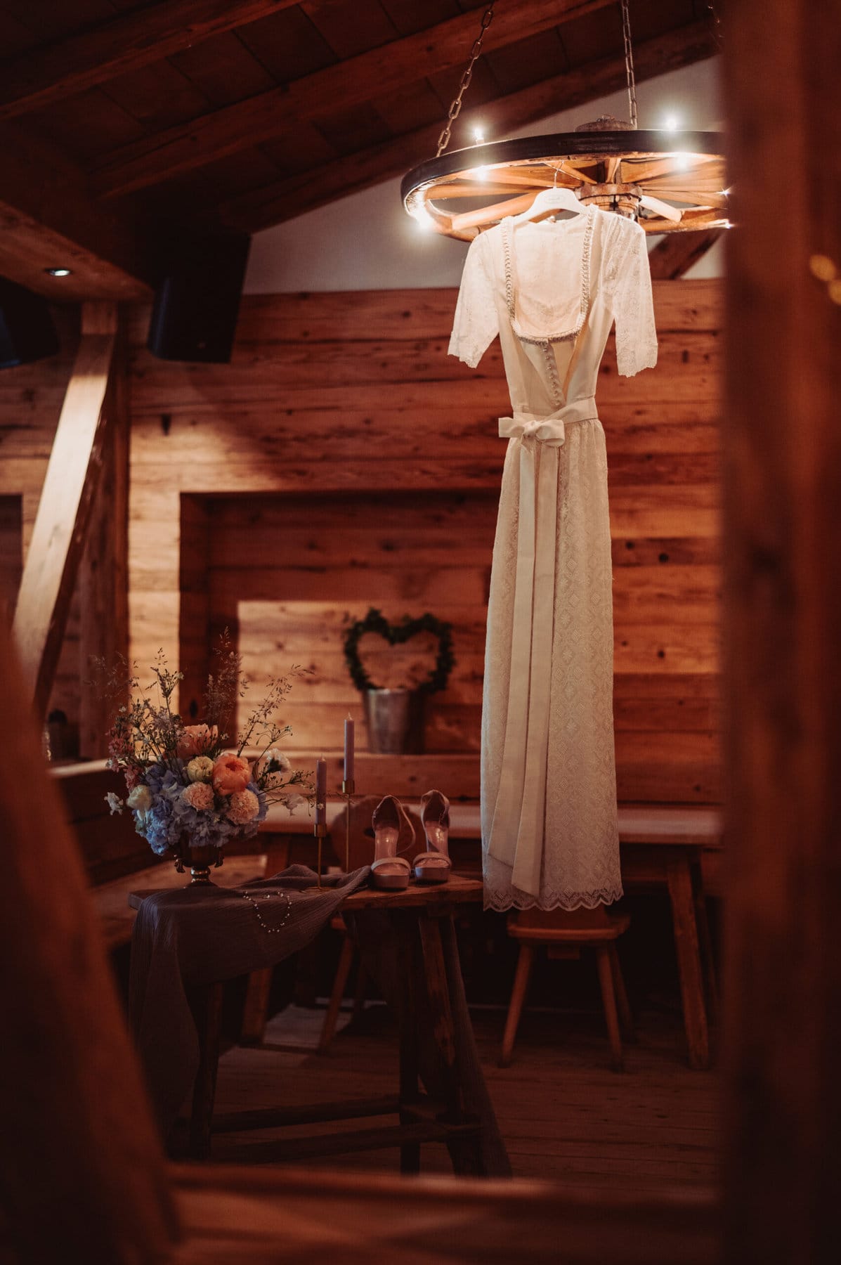 Das Getting Ready der Braut auf der Meckatzer Sportalp. In einem Raum aus Holz hängt das Brautkleid der Braut und auf einem kleinen Tisch stehen die Schuhe der Braut.