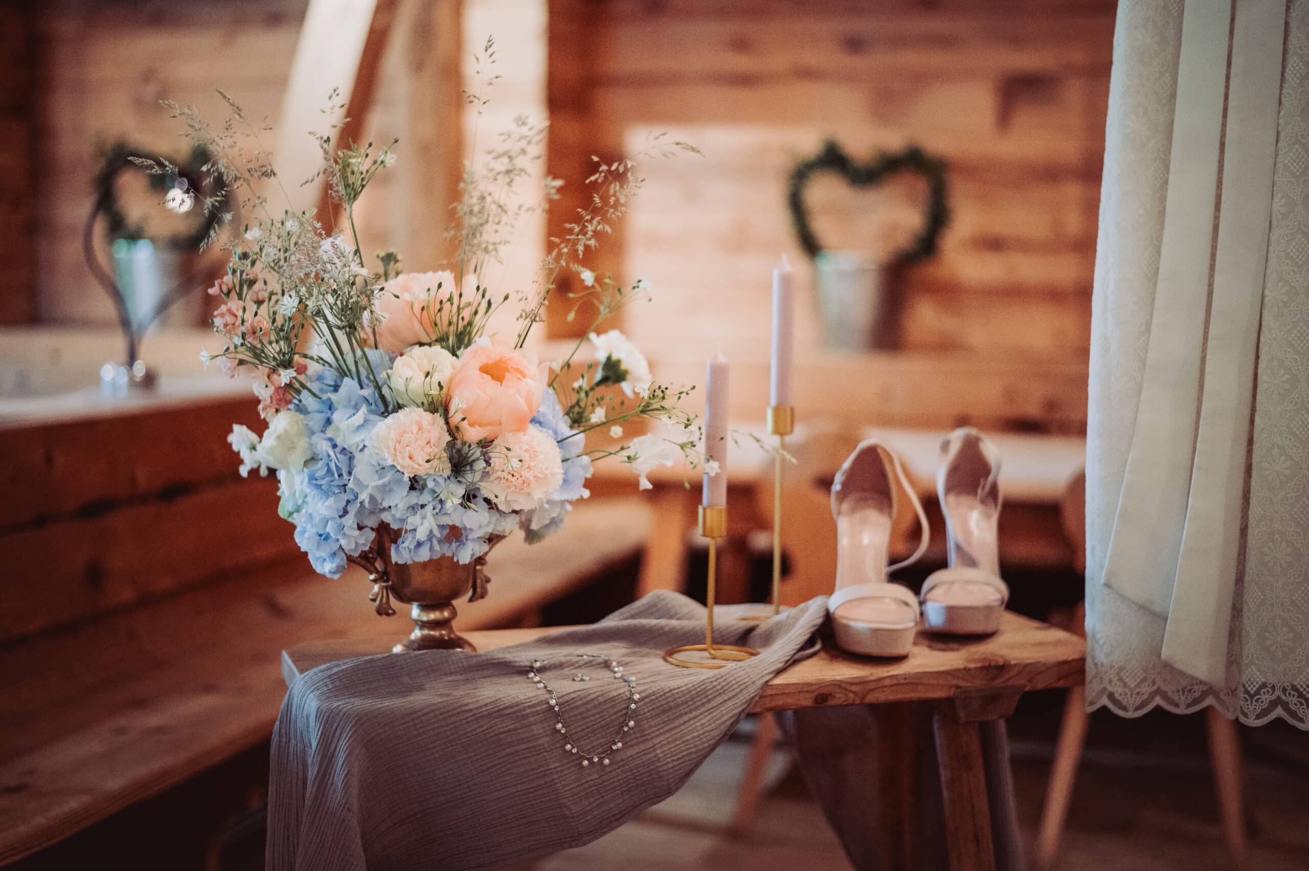 Das Getting Ready der Braut auf der Meckatzer Sportalp. Eine Nahaufnahme eines Beistelltisches mit einem Blumenstrauß, Kerzen und den Schuhen der Braut.