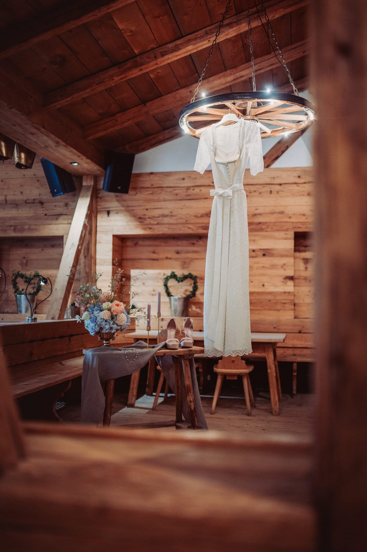 Das Getting Ready der Braut auf der Meckatzer Sportalp. In einem Raum aus Holz hängt das Brautkleid der Braut und auf einem kleinen Tisch stehen die Schuhe der Braut.