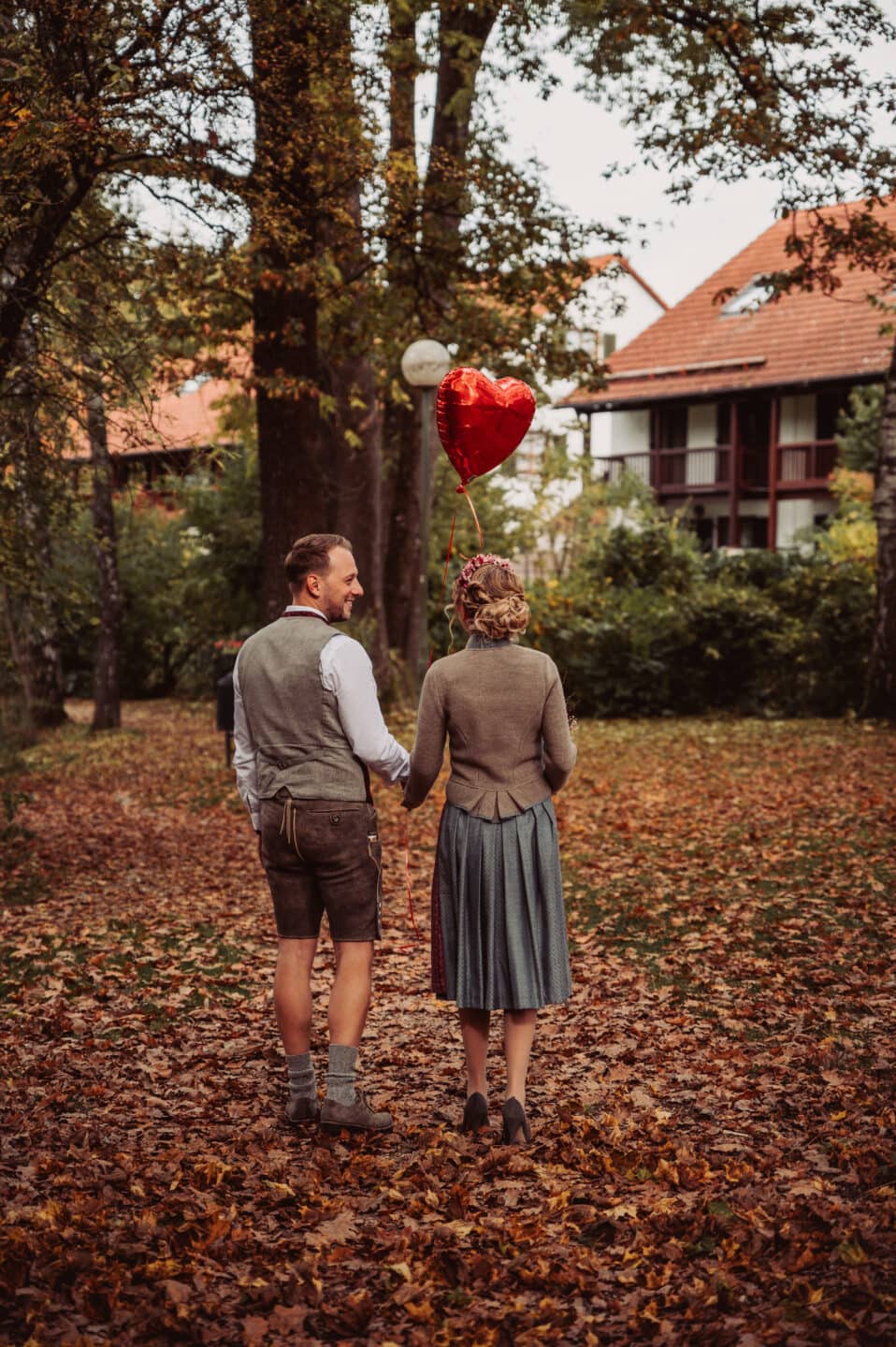 Das Brautpaar hält einen roten Herzluftballon beim herbstlichen Brautpaarshooting im Schmutterpark in Neusäß.