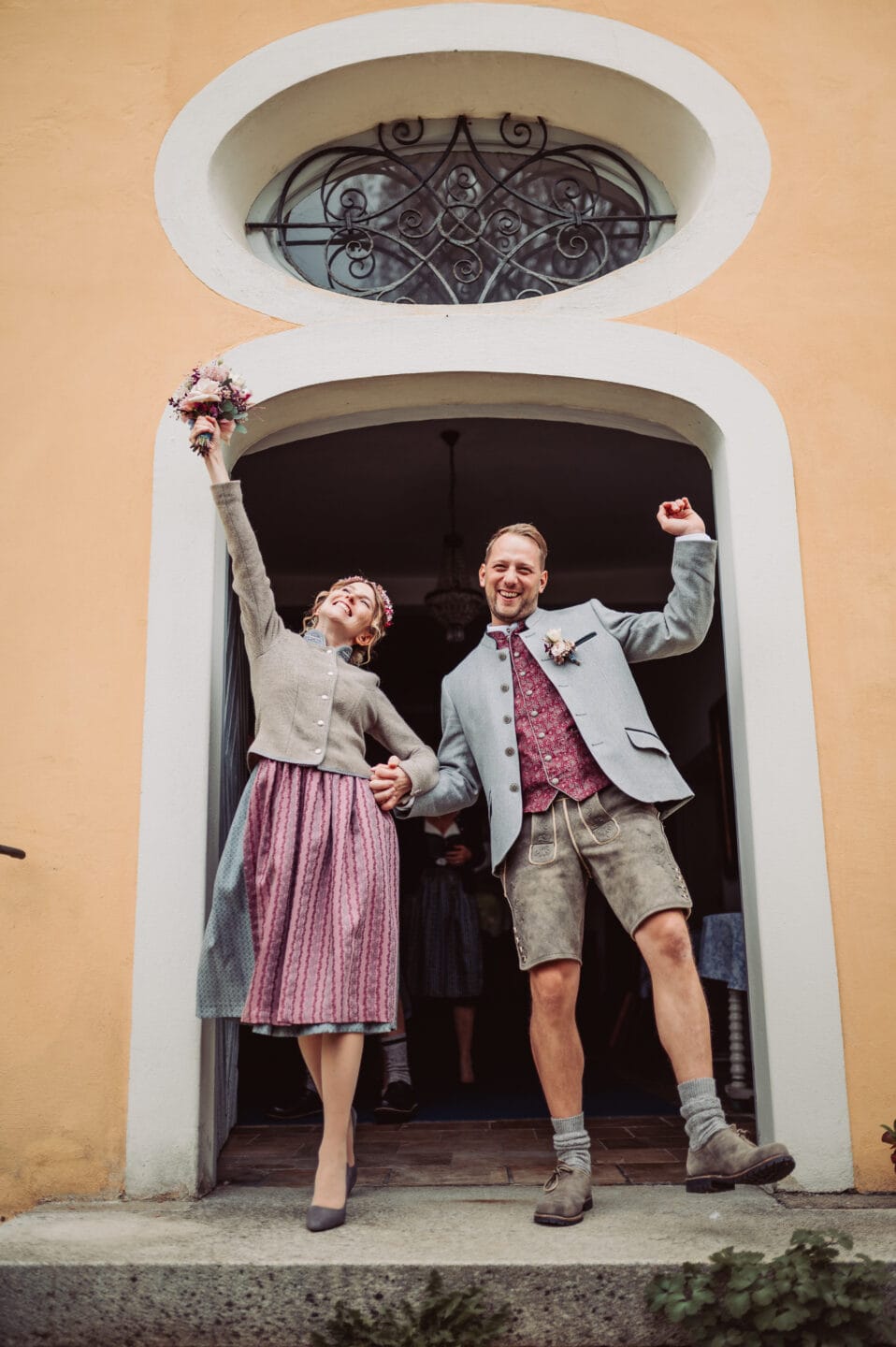 Das Brautpaar freut sich über die standesamtliche Trauung und hebt die Arme nach oben, als Zeichen der Freude am Ausgang des Schlosses in Aystetten.