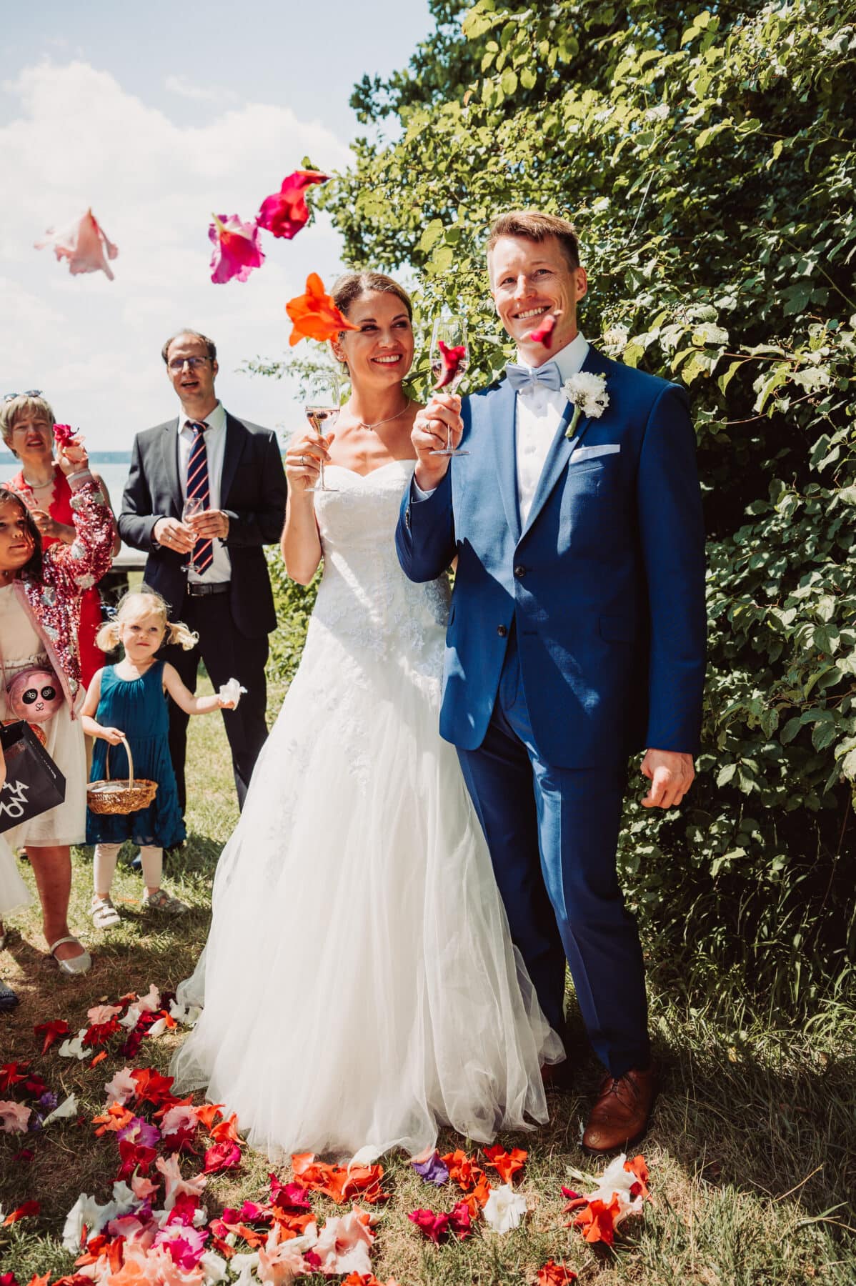 Das Brautpaar wird bei der Hochzeitsfeier am Starnberger See draußen im Garten vom Seewirt Buchscharner von den Kindern mit Blumen beworfen.