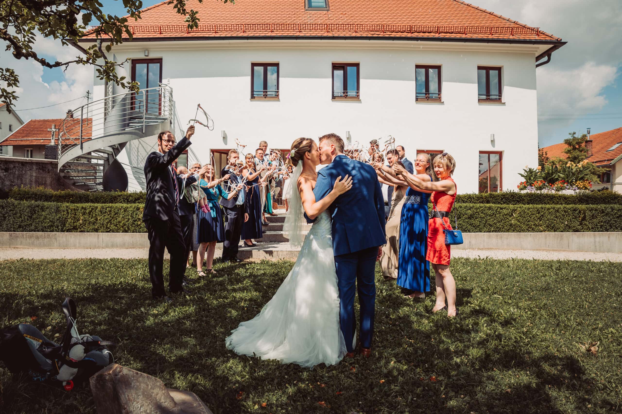 Das glückliche Brautpaar nach dem Standesamt in Pöking küsst sich vor den feiernden Gästen im Spalier bei der Hochzeitsfeier.